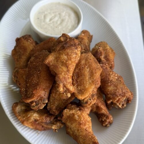 cooked trash wings on white plate next to dipping sauce