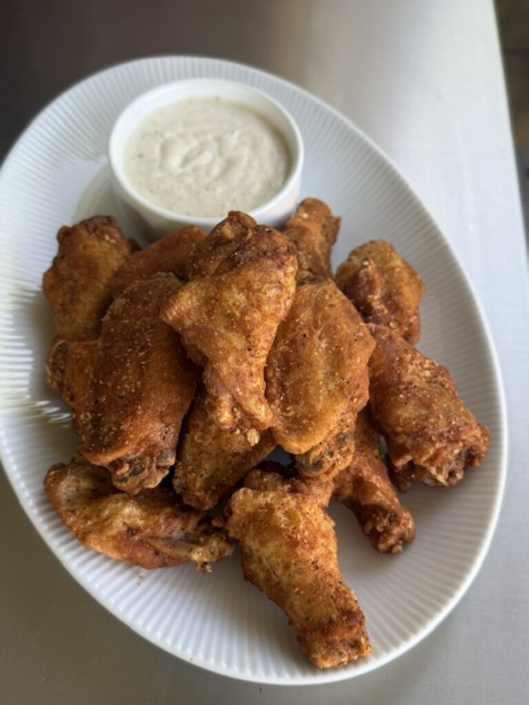 cooked trash wings on white plate next to dipping sauce