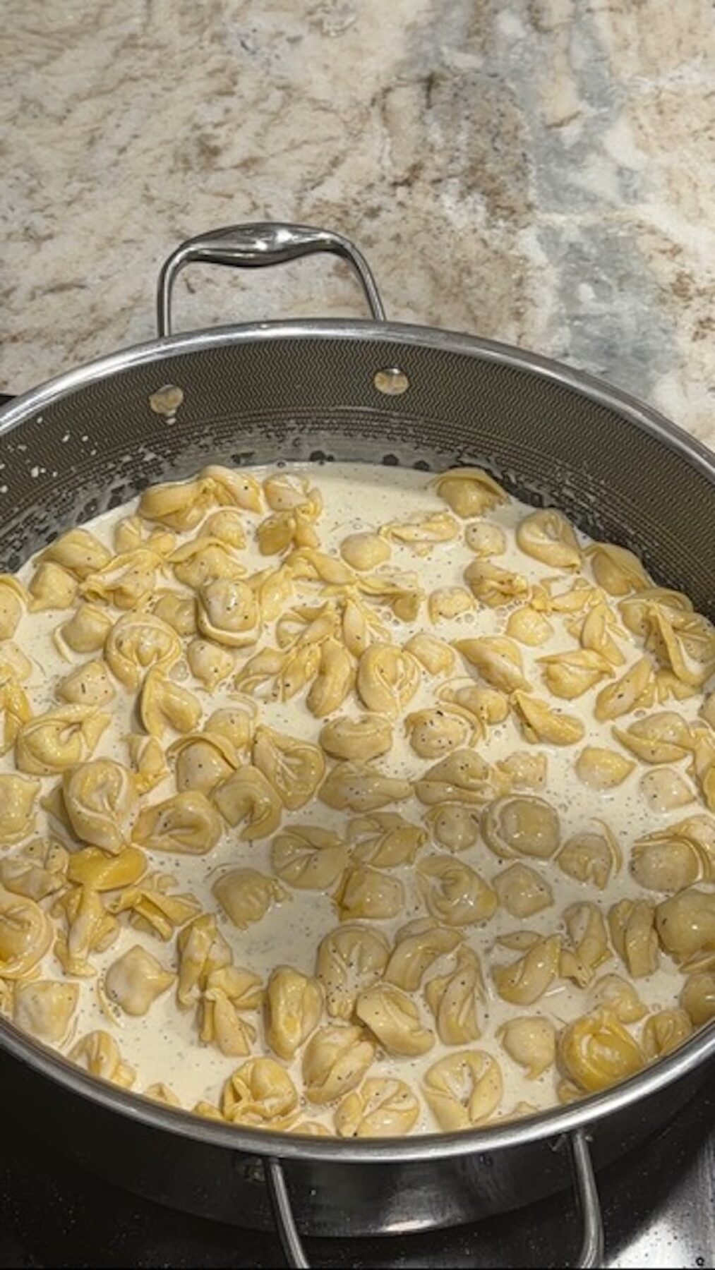 A pot with cream sauce and tortellini cooking.