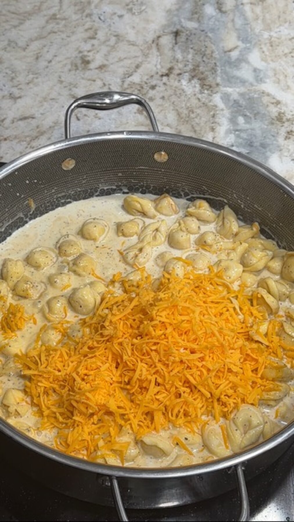 A black pot with tortellini and shredded cheese for chicken bacon ranch tortellini.