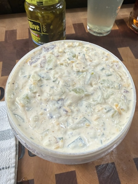 finished pickle dip in container with jar of pickled jalapeno slices in background