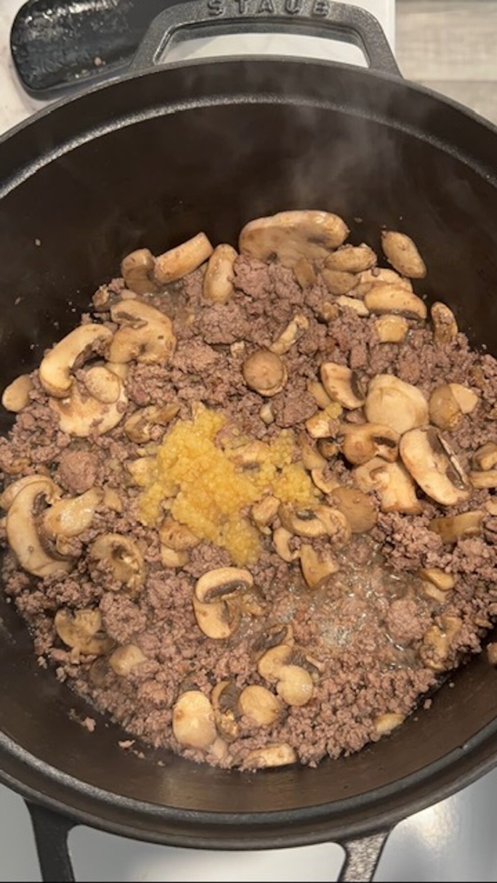 A pot with beef, mushrooms, and garlic cooking.