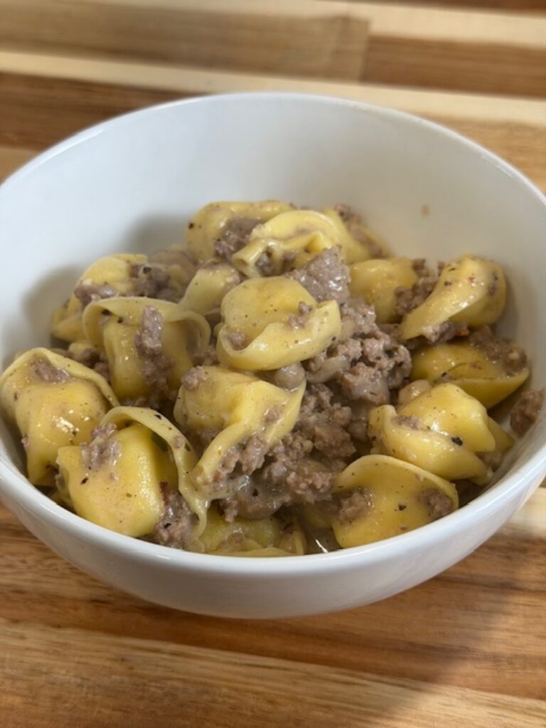 A white bowl with beef stroganoff tortellini.