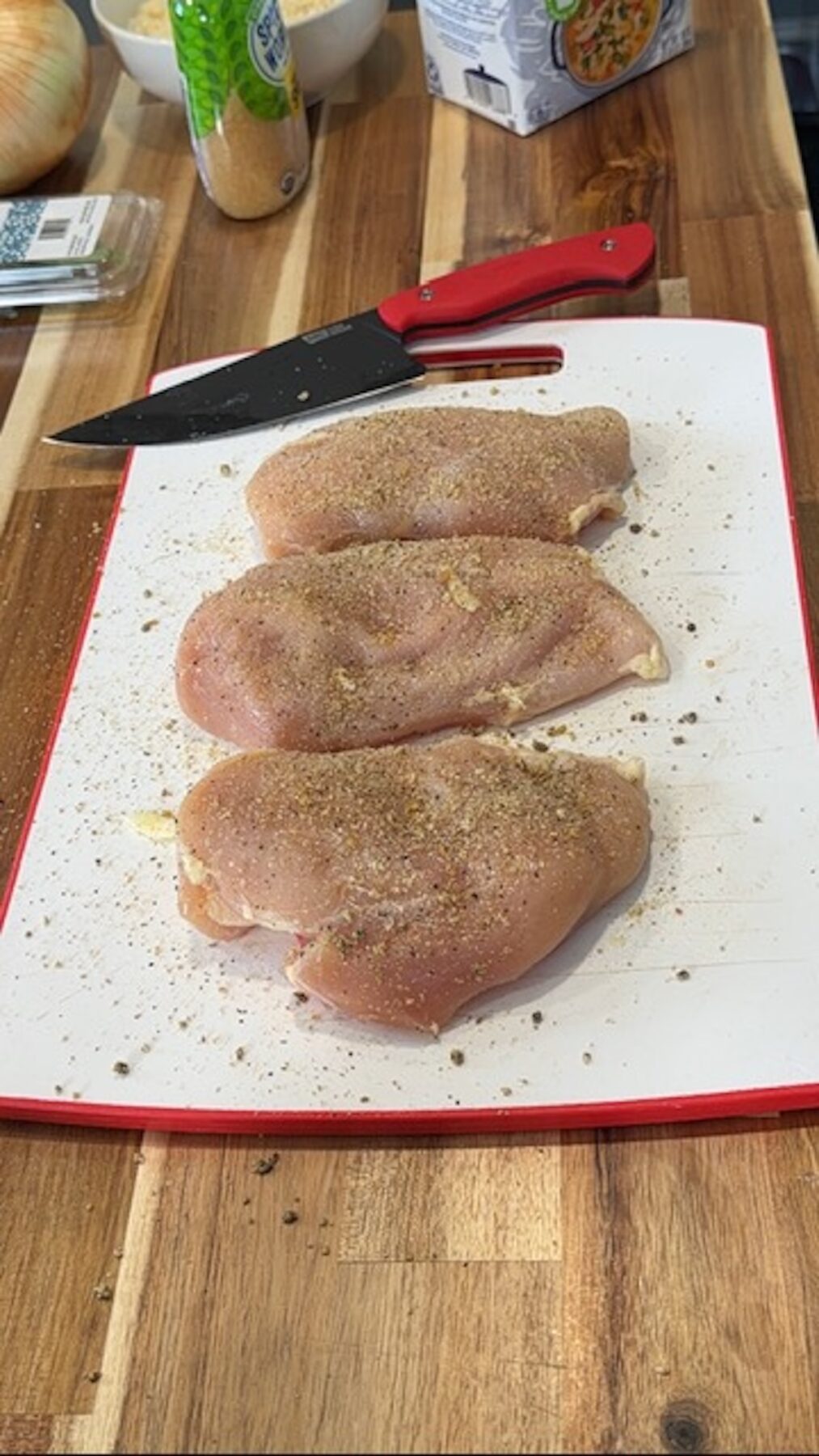 raw chicken breasts seasoned with spices on white cutting board with knife next to them
