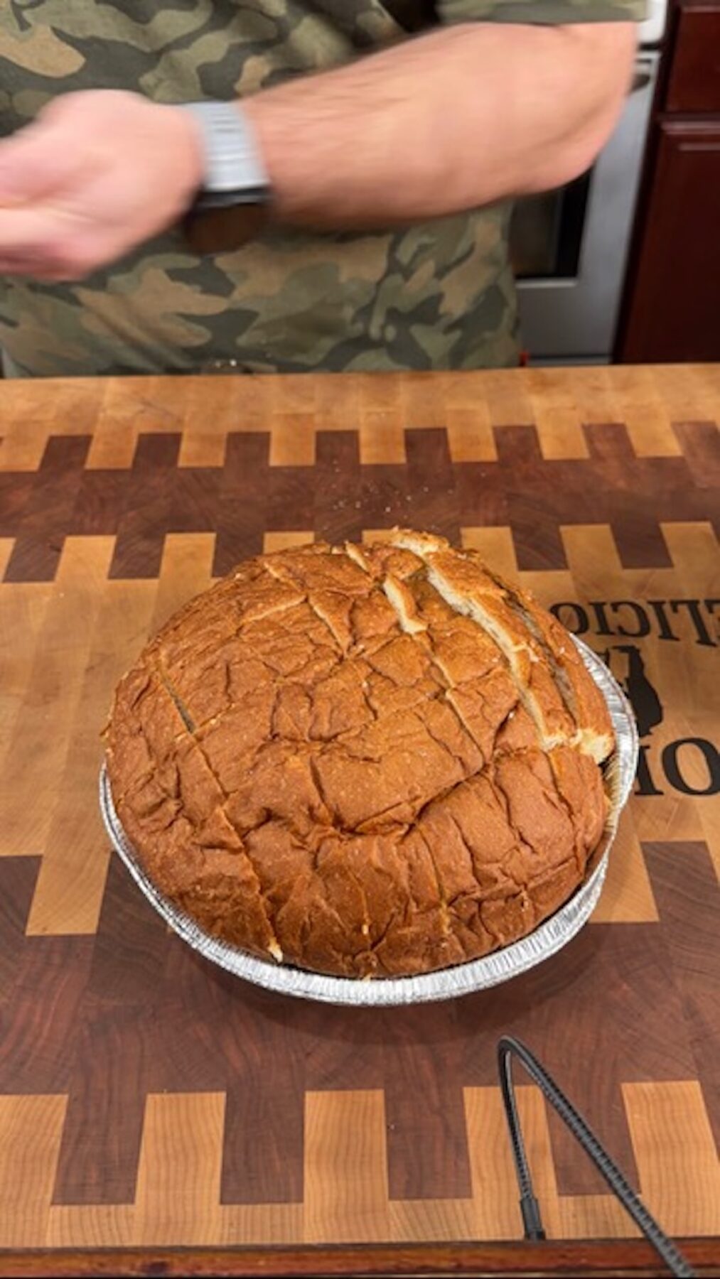 A loaf of bread with slits cut in it in a foil tin.