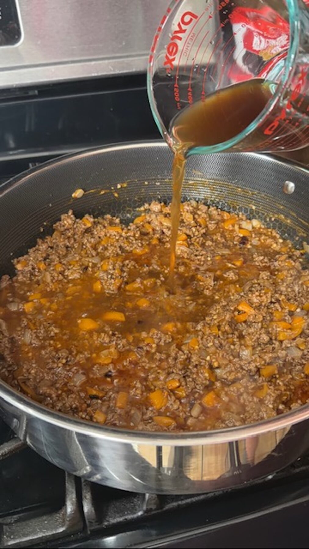 Beef broth and liquid being added to ground beef mixture in pan on stove