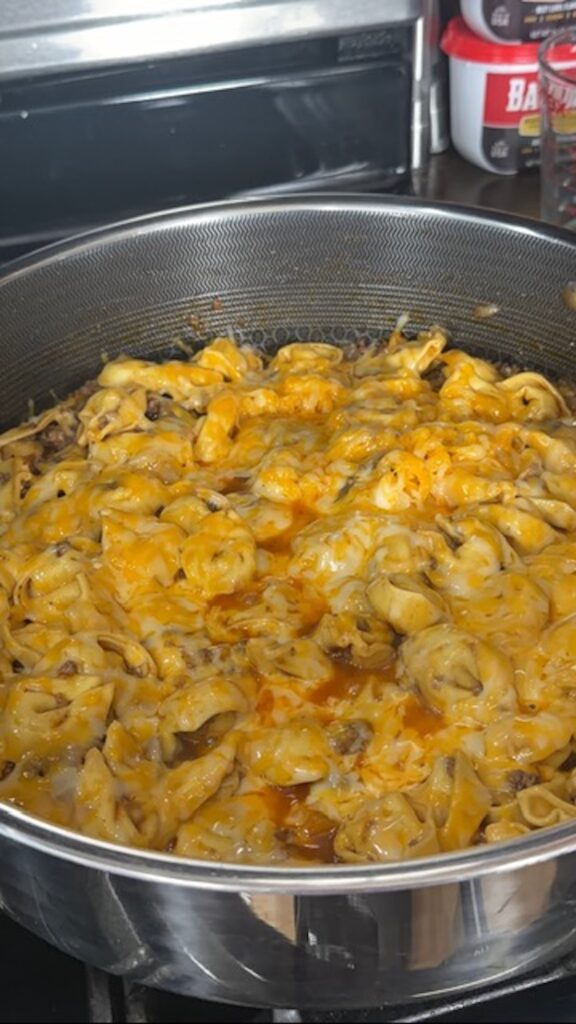 Sloppy joe tortellini cooked and topped with melted cheese in pan on stove